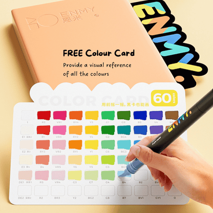 Color swatch card with a hand holding a pen and a notebook in the background. ENMY Black Box Soft Tip Acrylic Markers